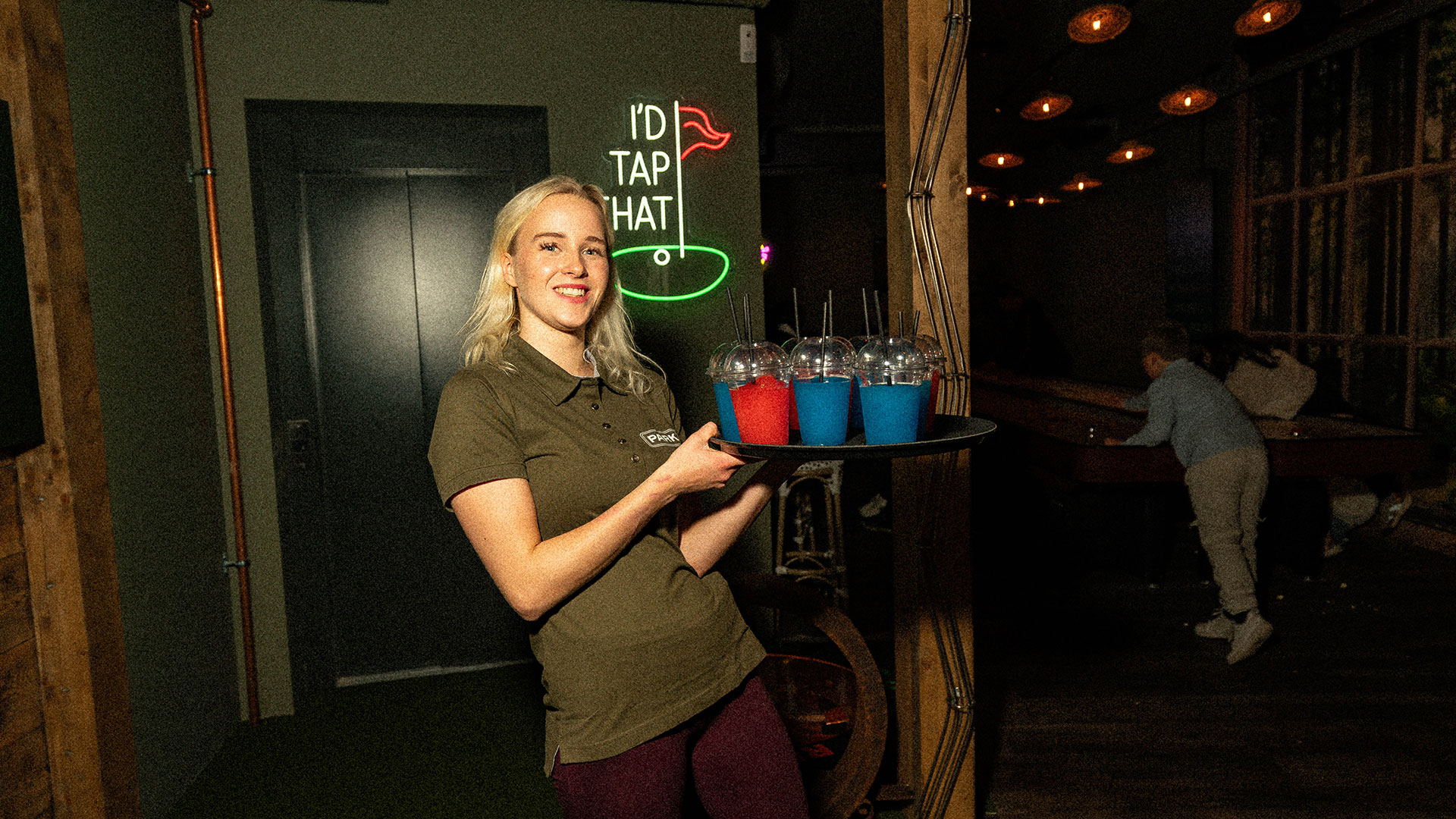 Servitør med slush-brett på ParkN — krem-uniform og safran-aksent